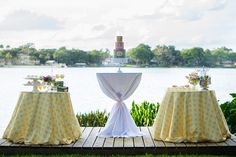 two tables with yellow and white tablecloths are set up on a deck near the water