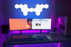 two computer monitors sitting on top of a desk in front of a purple background with hexagonal shapes