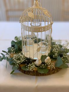 a birdcage filled with candles and greenery on top of a white table