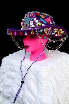 All eyes will be on you in this fabulous purple cowgirl hat covered to the brim with rainbow galore. From the front hang colorful gummy bears and from the sides hang three colorful beaded chains. The hat is covered with stars, hearts, flowers, rhinestones, butterflies, pearls, disco balls, mini animals and treats, and silver tinsel. It has a purple and lace neck tie. Fun Adjustable Hat For Carnival, Funky Adjustable Party Hats, Fun Carnival Costume Hats And Headpieces, Multicolor Beaded Party Hats, Fun Adjustable Mini Hats For Carnival, Fun Festival Costume Hats And Headpieces, Adjustable Wide Brim Hat For Carnival, Trendy Adjustable Costume Hats And Headpieces For Festival, Fun Carnival Festival Costume Hats And Headpieces