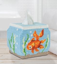 a tissue box with a goldfish design on the front and bottom, sitting on a wooden table