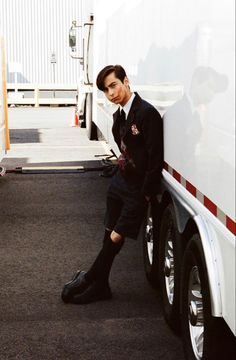 a man in uniform leaning against the side of a semi truck with his foot on the ground