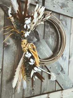 a wreath with dried flowers and feathers hanging on a wooden door hanger next to a rope