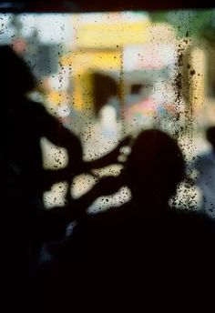 the shadow of a person standing in front of a window with rain drops on it