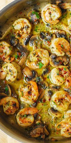 a pan filled with shrimp, mushrooms and olives on top of a wooden table