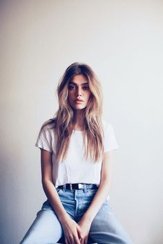 a woman sitting on top of a suitcase wearing blue jeans and a white t - shirt