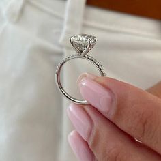 a woman's hand holding a diamond ring in front of her face, with white pants