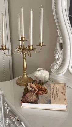 a white dresser topped with a book next to a candelabra filled with candles