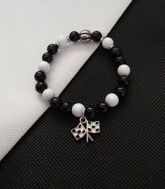 You will love this stretch beaded bracelet designed with black and white 8mm glass beads, silver accents along with a black and white check flag charm.  The stretch will fit most sizes and is approximately 7" prior to tie closure.  The adorable charm was purchased on Etsy and is sure to please.  If you need a different size, please send me a message.  The black and white flag is approximately 18mm x 16mm with 2mm thickness, zinc alloy enamel. This charm gives the appearance of blowing in the wind.  It's very unique. My shop offers combined shipping.  Purchase multiple items on one invoice and pay one flat shipping fee.  This is a great deal for shoppers! All items in my shop intended for adults only. All items in my shop contain small parts and may pose a choking hazard to children and oth Cheap Themed Black Charm Bracelet, Handmade Themed Black Bracelets, White Stretch Bracelet With Black Beads Gift, Black Beaded Rave Bracelets, Adjustable Black Beaded Punk Bracelets, Red Black White Bracelet, Black And White Flag, Black And White Jewelry, Flag Bracelet