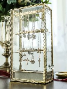 a glass display case filled with jewelry on top of a table next to a vase