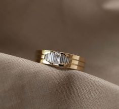 a gold ring with three baguettes sitting on top of a beige material surface