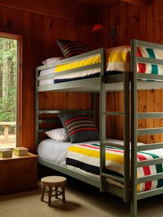 a bunk bed sitting next to a window in a wooden room with wood paneling