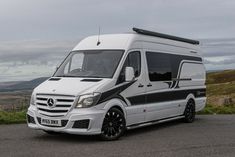 a mercedes benz camper van parked on the side of a road with mountains in the background