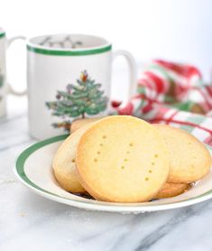 some cookies are on a plate next to two mugs