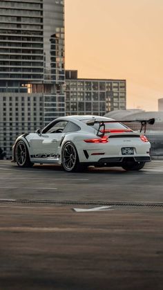 a white sports car parked in front of tall buildings on an airport tarmac at sunset