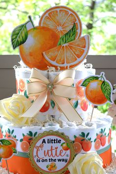 a three tiered cake decorated with oranges and flowers on the top is an ad for a little cutie it's on the way