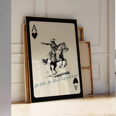 an ace playing card sitting on top of a wooden floor next to a framed poster