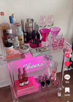 a pink bar cart with liquor bottles and glasses on it's side, in front of a white wall