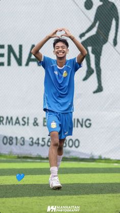 a young man holding a soccer ball on top of his head in front of a sign