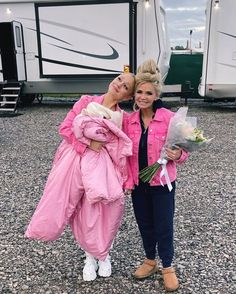 two women standing next to each other in front of a trailer with flowers on it