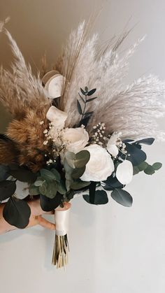 a bridal bouquet with feathers, flowers and greenery on the wall behind it