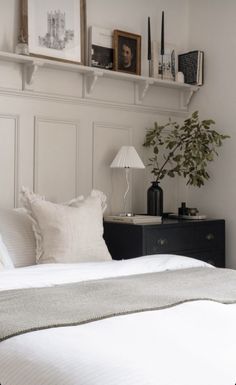 a bed with white sheets and pillows next to a wall mounted shelf filled with pictures