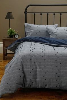 a bed with grey and blue comforter on it in a bedroom next to a wooden floor