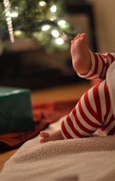 a baby sitting on the floor in front of a christmas tree with its feet up