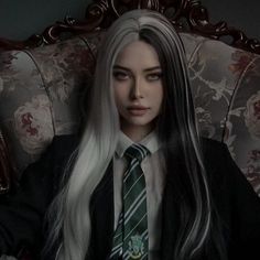 a woman with long white hair wearing a tie and sitting on a chair in a dark room