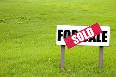 a for sale sign sitting in the middle of a green field with grass behind it