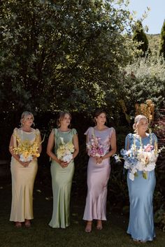 three women in dresses standing next to each other with flowers on their heads and holding bouquets