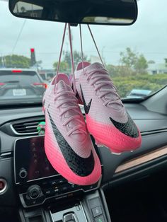 pink and black nike shoes hanging from the dashboard of a car