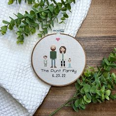 a cross stitch pattern with two people and a heart on it, next to some green leaves