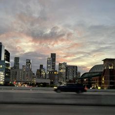 the city skyline is lit up at night as seen from across the street with cars driving by