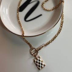 This necklace is made with a classy 18" figaro chain, a toggle clasp to wear in the front, and finished with a checkered pendant. Care instructions: To prolong the lifetime of your item, avoid direct and prolonged contact with harsh chemicals, chlorinated pools, perfumes and lotions. Your jewelry can be cleaned with lukewarm water and a small amount of mild soap. Let it soak for 3-5 minutes and dry with a soft cloth. If you feel the need to deep clean, you can use a soft (preferable baby soft) t Metal Chunky Chain Toggle Necklace Gift, Gift Metal Toggle Necklace With Chunky Chain, Chunky Chain Toggle Necklace Metal Gift, Gift Toggle Necklace With Chunky Chain, Trendy Gold Rectangular Necklaces, Trendy Gold Rectangular Necklace, Everyday White Rectangular Pendant Necklace, Trendy Charm Necklaces With Lobster Clasp For Everyday, Trendy Gold-tone Charm Necklace As Gift