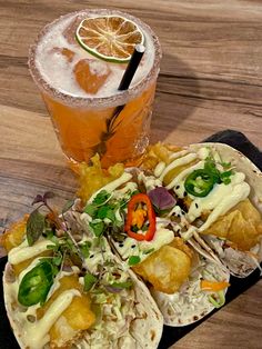 two tacos and a drink sitting on a table next to each other with orange slices