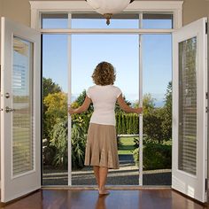 a woman standing in front of an open door with her hands on the glass doors