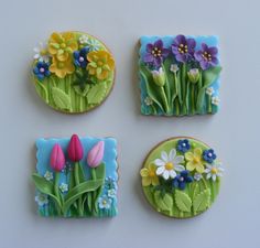 four decorated cookies sitting on top of a white table covered in icing and flowers