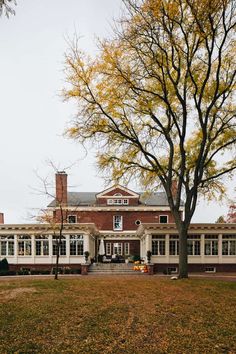 a large red brick house sitting on top of a lush green field next to a tree