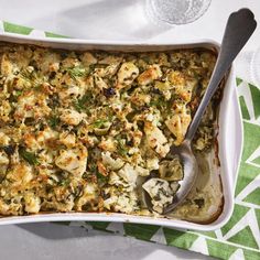 a casserole dish with chicken and vegetables in it on a green napkin next to a silver spoon