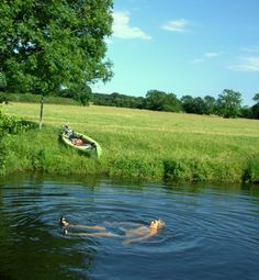 a man floating on top of a body of water next to a green boat in the middle of a field