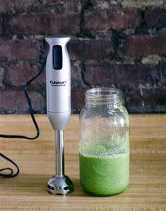 a blender sitting on top of a wooden table next to a jar filled with green liquid