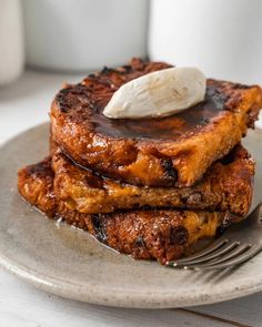 two pieces of french toast topped with butter and syrup on a plate next to a cup