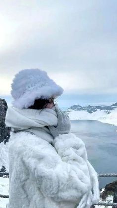 a woman standing on top of a snow covered slope next to a lake in the middle of winter