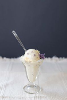 an ice cream sundae with purple flowers in a clear glass cup on a white tablecloth