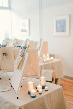 an easel and some candles on a table in a room with white linens