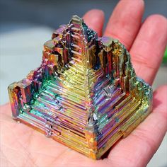 a hand is holding a colorful crystal pyramid