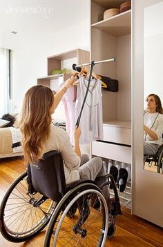 a woman in a wheel chair hanging clothes on a rail next to a bed and closet