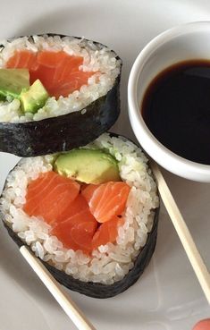 two sushi rolls with avocado, salmon and rice on a white plate