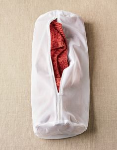 an unzipped white bag with red lining on the inside is laying on a beige surface